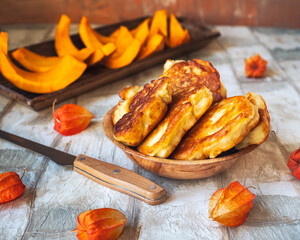 Pumpkin pancakes in a deep plate and slices of raw pumpkin on an oblong wooden tray