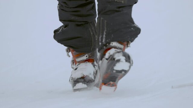 feet in ski boots go through deep snow towards the camera
