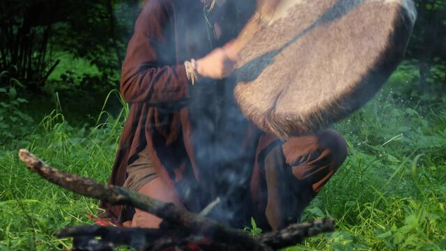 Female shaman drumming in a trance at night in the forest by the fire
