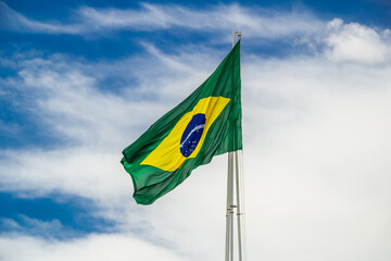 Bandeira do Brasil hasteada e tremulando com o vento e céu com nuvens ao fundo.