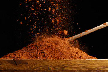 Falling cocoa powder on wooden table and spoon. Shallow depth of field