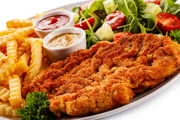 Breaded fried pork chop, French fries and vegetables on white background
