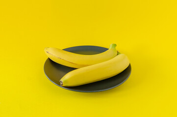 Ripe banana on black plate on yellow background. Tropical fruits for eating