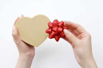 Women's beautiful hands hold a gift box and a red bow on a white background. The concept of preparing for a birthday, Valentine's day, mother's day, wrapping a gift in a gift box-craft with a red bow.