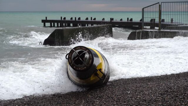 A large black and yellow buoy washed ashore after a storm. A broken sea buoy lies on the shore against the backdrop of the sea after a storm.