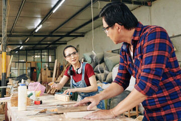 Female carpenter asking experienced colleague to help her with advice on making even planks for furniture item