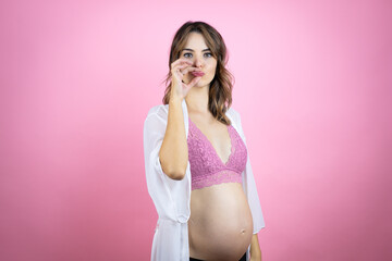 Young beautiful brunette woman pregnant expecting baby over isolated pink background mouth and lips...