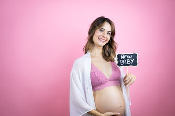 Young beautiful brunette woman pregnant expecting baby over isolated pink background smiling and holding blackboard with new baby word message