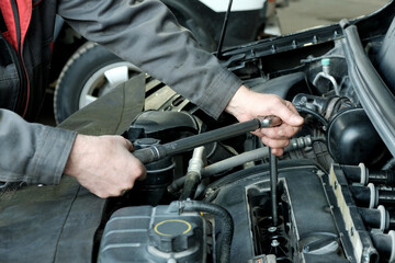 Maintenance and repair of cars in the service center. Close-up of the hands of a mechanic performing a torque wrench rotation of the bolts securing the engine cylinder head cover.