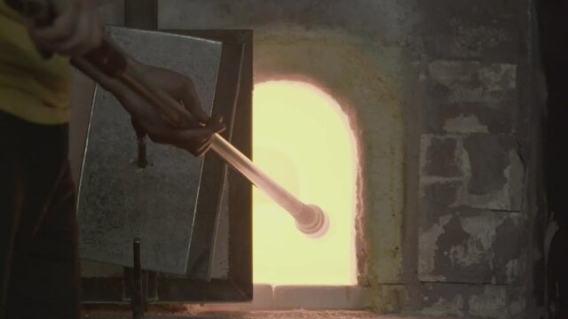 Medium Shot of Man Opening Kiln and Inserting Blown Glass