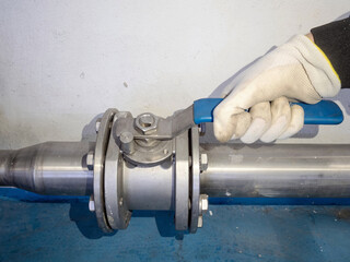 Hand with safety glove opened ball valve on silver stainless pipe