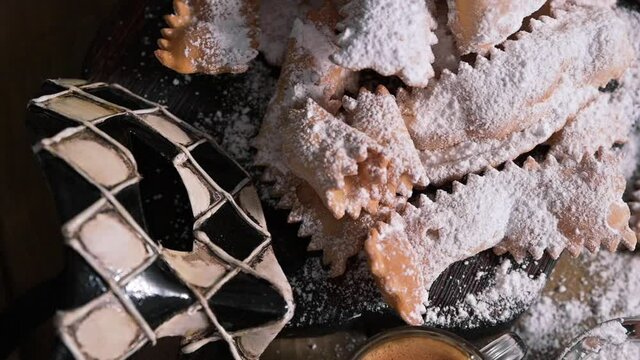 Carnival food TYPICAL and carnival mask. Sfrappole or chiachiere or angel wings and aromatic coffee on a woody background. Traditional sweet crisp pastry deep-fried and sprinkled with powdered sugar. 