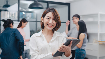 Portrait of successful executive businesswoman smart casual wear looking at camera and smile with digital table in modern office workplace. Young Asia lady standing relax in contemporary meeting room.