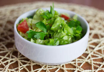 Green lettuce salad in a white bowl with tomato