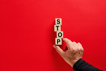 Male hand arranging the wooden blocks with the word stop on red background with copy space....