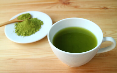 Closeup a Cup of Hot Matcha Green Tea on Wooden Table with Blurry Matcha Tea Powder in Background