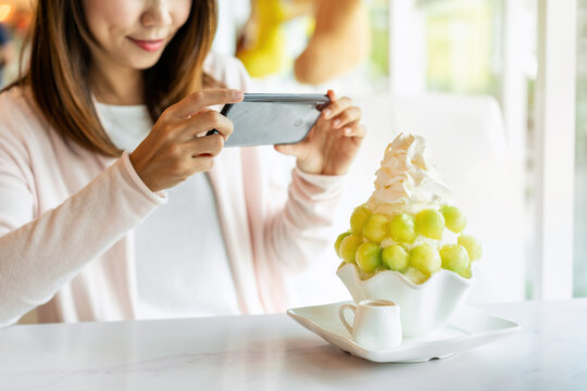 Young woman taking photo of bingsu with smart phone in restaurant and uploading the photos to the social media