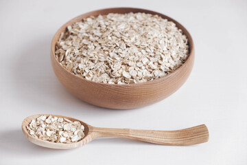 Dry oatmeal in a wooden plate and spoon on a white background. Top view. Copy, empty space for text
