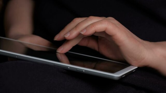 Hand of a woman who is viewing the news on a tablet close-up on a black background