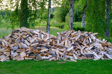 A large pile of firewood on the meadow. Trees has been cut and split into firewood to be used as fuel for heating in fireplaces and furnaces . Selective focus