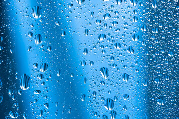 Abstract background ornament with water drops.Raindrops on the glass in rainy weather.The glittering, shiny surface of water on glass.Water drops in the form of balls or spheres.Blue raindrops