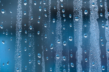 Naklejka na ściany i meble Raindrops on the glass in rainy weather.The glittering, shiny surface of water on glass.Water drops in the form of balls or spheres.Blue raindrops background. Abstract backgrounds ornament with water