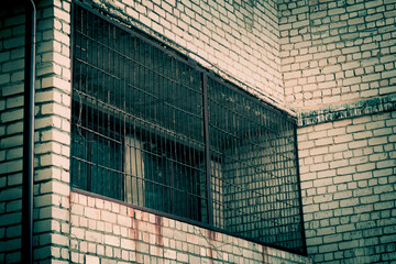 Gloomy background with brick wall surface texture with scary window with metal rusty grating on the balcony in horror style with scary shadows and mystical light