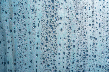 Raindrops on the glass in rainy weather.The glittering, shiny surface of water on glass.Water drops in the form of balls or spheres.Blue raindrops background. Abstract backgrounds ornament with water