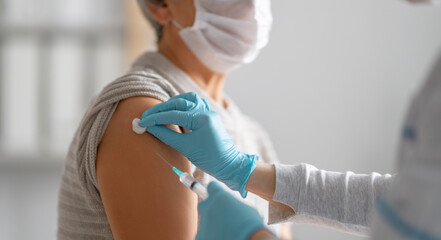 Doctor giving a senior woman vaccination - obrazy, fototapety, plakaty