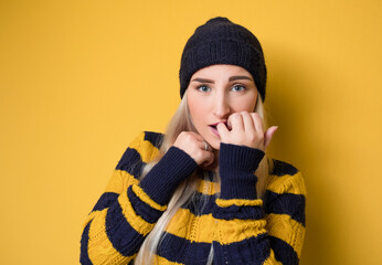 Scared young woman biting fingernail,being terrible accident, model wearing woolen cap and sweater,...