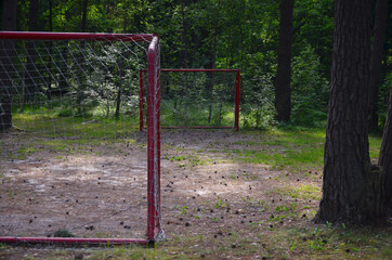 Fototapeta na wymiar Red football goal with a net in a forest park at a recreation center in summer