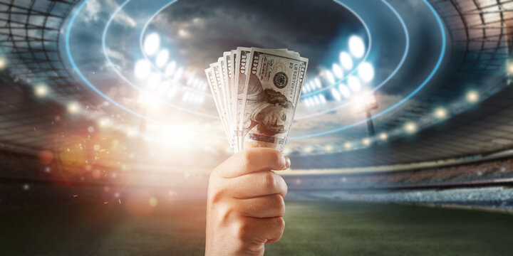 Close-up of a man's hand holding US dollars against the background of the stadium. The concept of sports betting, making a profit from betting, gambling. American football.