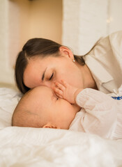 Fototapeta na wymiar mom kisses her daughter on the white blanket on the bed