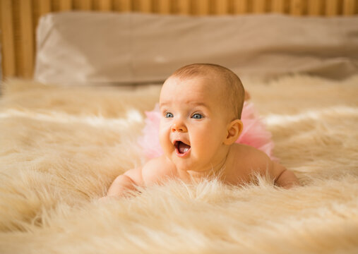 happy baby girl in pink panties lies on a beige fluffy blanket