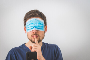 Conspiracy theory concept: Young man with face mask over the eyes is making a psst! gesture