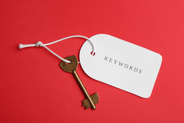 Metal key and tag wIth word KEYWORDS on red background, top view