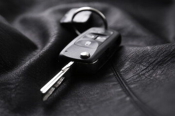 Modern car flip key with trinket on black leather, closeup