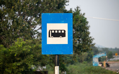 Clear closeup photo of Indian National Highways Bus Stop Road Sign Board with Blue white background and Bus Logo in black colour in middle with only bus stop in background where people get on to Bus