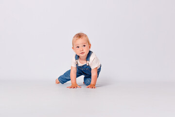 Cute year-old baby girl in a blue denim jumpsuit sits on white background. a child's photo shoot