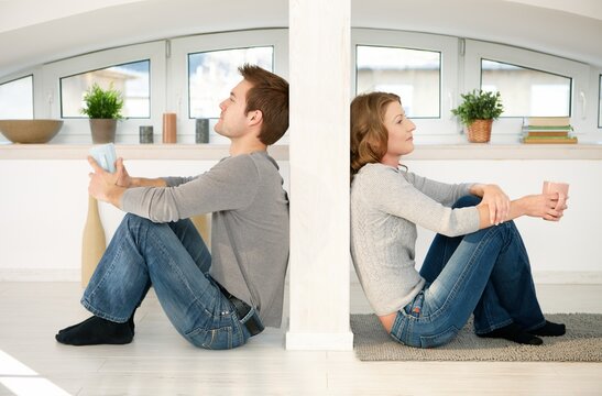 Couple sitting on floor at home resting, drinking coffee.