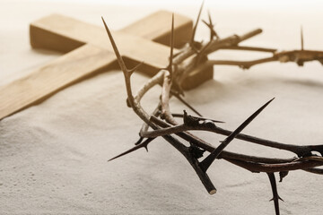 Crown of thorns and wooden cross on sand, closeup. Easter attributes