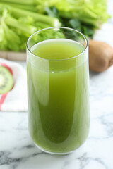 Glass with fresh celery juice on white marble table, closeup