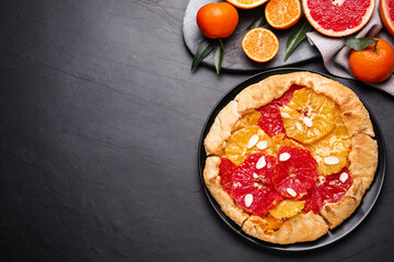 Tasty galette with citrus fruits on dark grey table, flat lay. Space for text