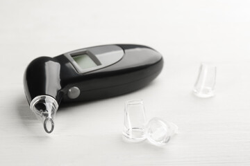 Modern breathalyzer and mouthpieces on white wooden background