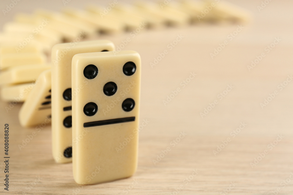 Wall mural White domino tiles falling on wooden table, closeup. Space for text