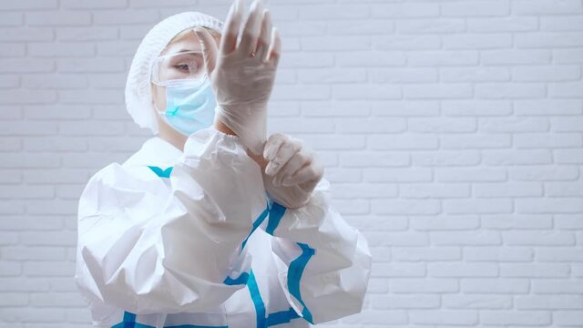 Nurse in protective clothes putting on disposable gloves for injection.