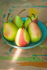 Green pears with red sides lying on a turquoise plate on the table in watercolor paint.
