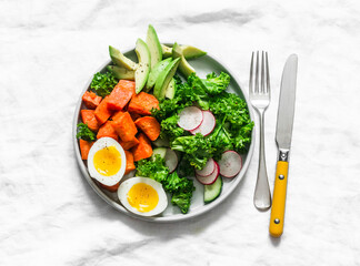 Vegetarian lunch - boiled sweet potatoes, egg, kale, avocado, radish, cucumber salad on a light background, top view