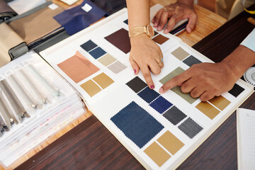 Hands of tailor and client choosing fabric from catalog for making bespoke suit