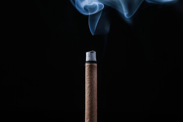 Incense stick smoldering on black background, closeup
